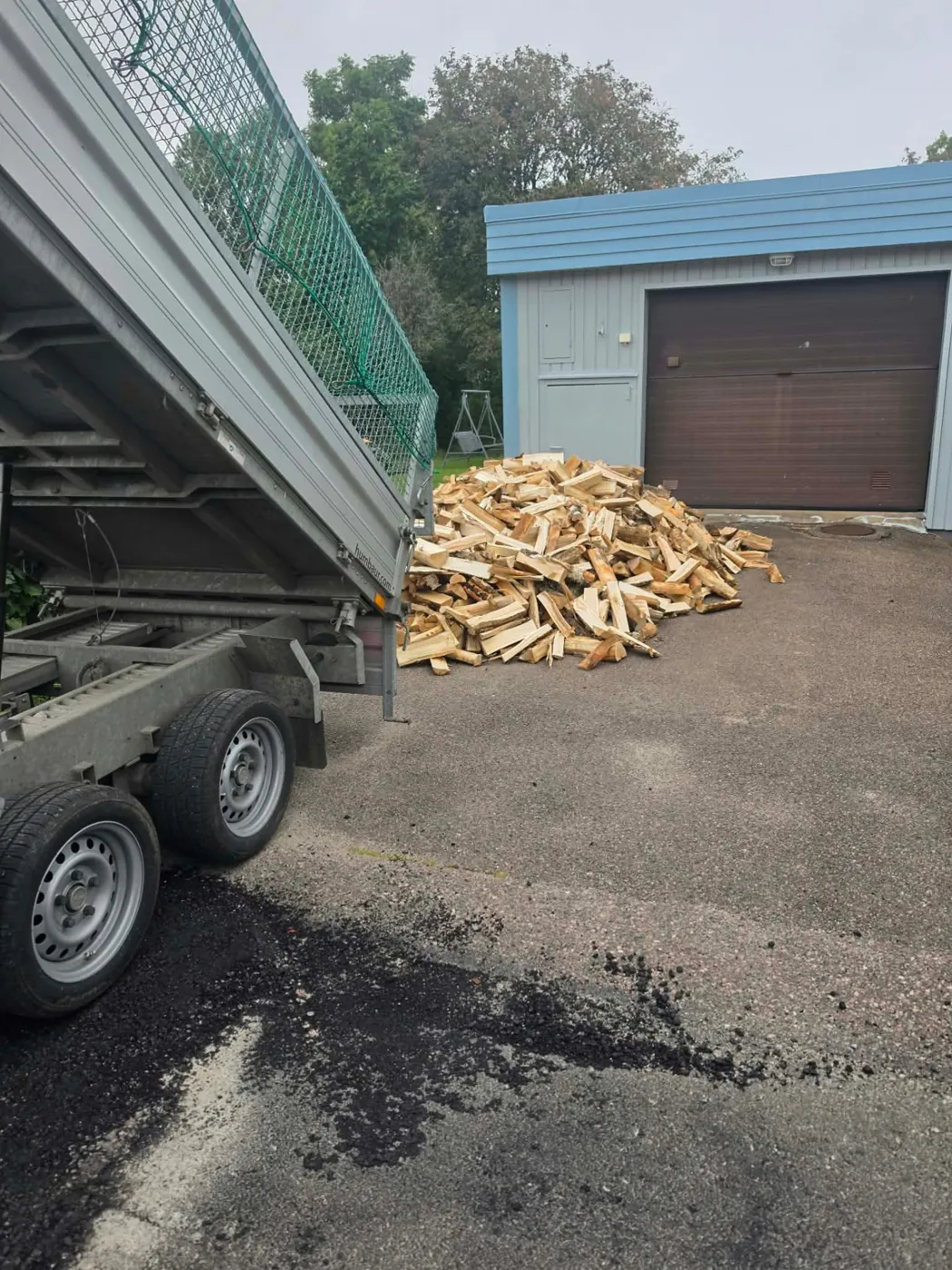 Hög med kluven ved tippad på en asfalterad uppfart framför ett garage